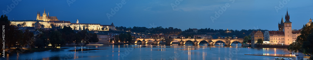 Prague riverside at night. Panoramic image of illuminated Charles Bridge and Novotnevo Lavka riverside buildings with a clock tower