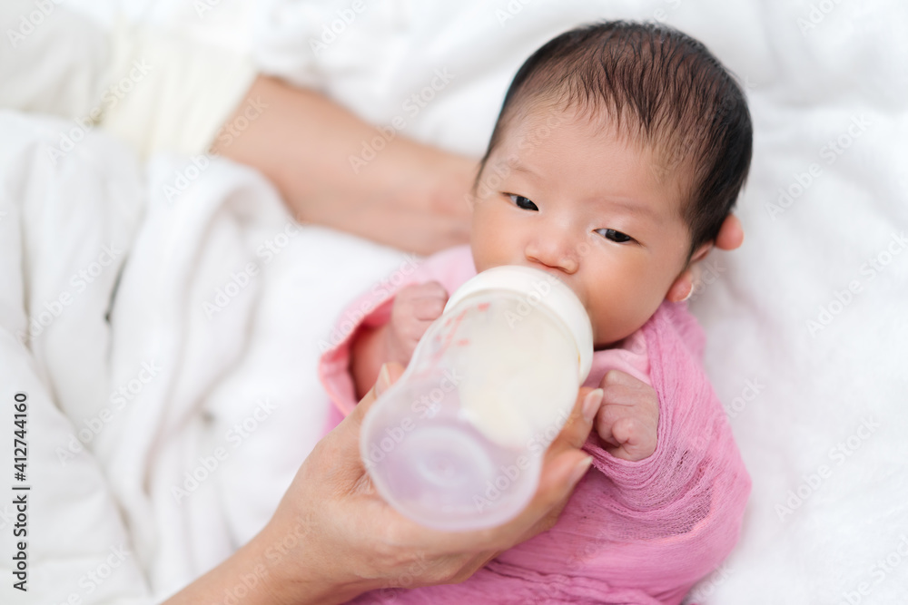 mother feeding milk bottle to her newborn baby on bed mother feeding milk bottle to her newborn baby on bed