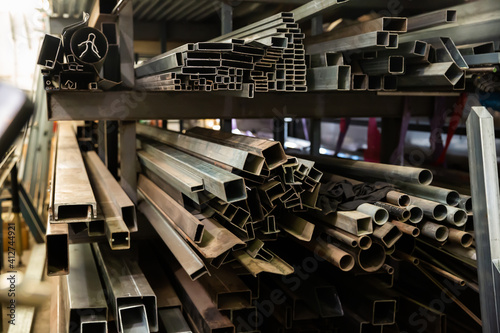 Variety of iron square tubes, round pipes and shaped profiles on rack in metalworking shop..