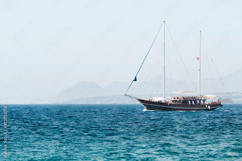 Naklejka premium A touristic yacht with tourists in sea. Summer beautiful trip in the sea in the morning sunlight.