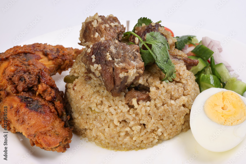 Beef Biryani Tehari with boiled egg coriander leaf garnish chicken curry pot roasted leg tomato cucumber onion chili coriander salad on white plate set over white background Beef Biryani Tehari with boiled egg coriander leaf garnish chicken curry pot roasted leg tomato cucumber onion chili coriander salad on white plate set over white background