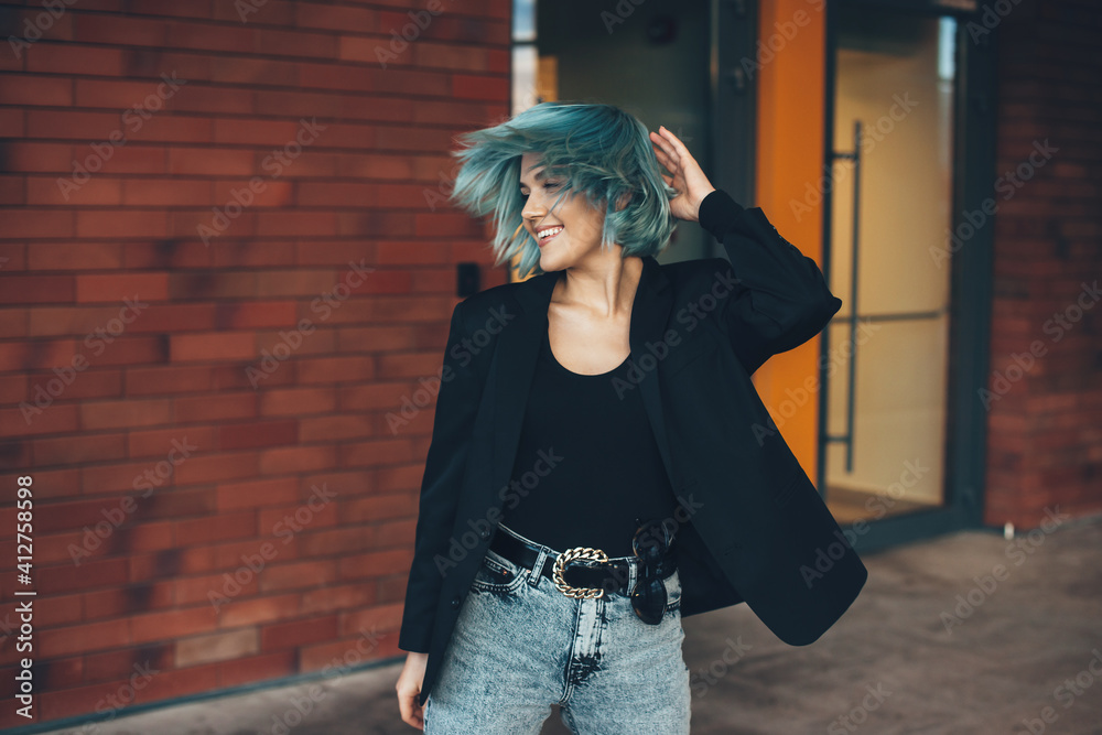 Cheerful caucasian woman with blue hair is shaking head posing outside on a  brick wall dressed in jeans and suit Stock Photo | Adobe Stock