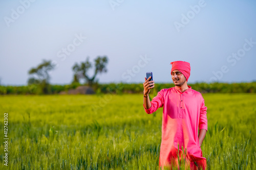 Young indian farmer takeing selfie in smartphone at green wheat field