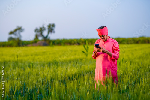 Young indian farmer using smartphone at wheat field