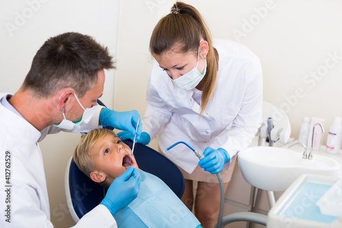 Stomatologist guy with woman assistant are diagnosticating to young patient which is sitting in dental clinic.