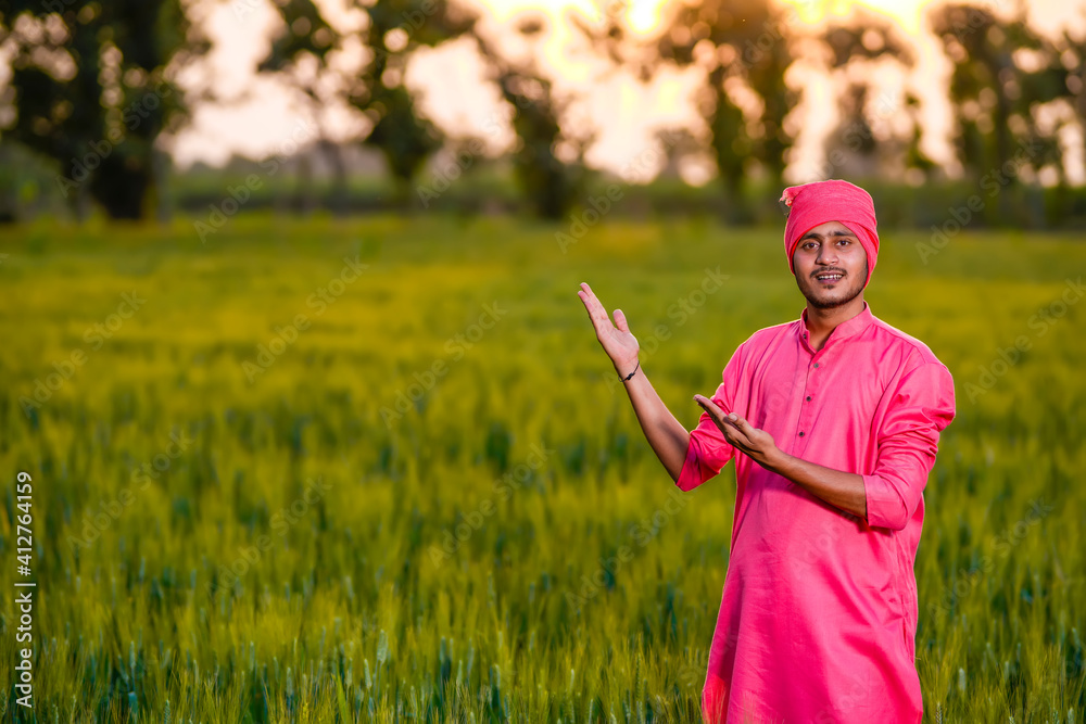 Young indian farmer standing at green wheat field