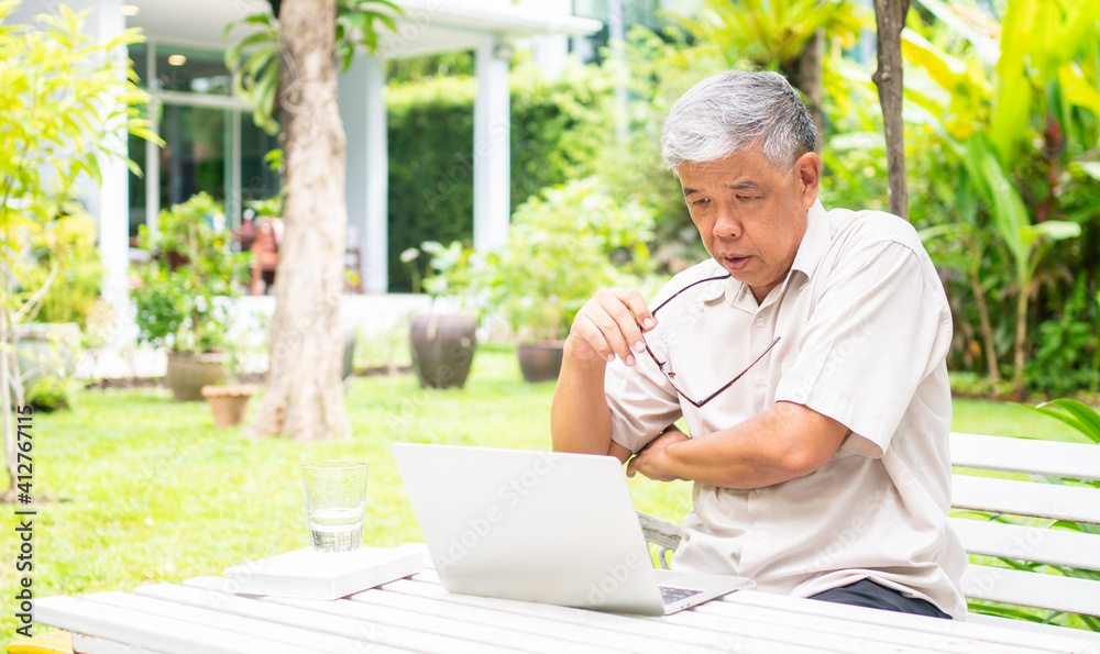 Obraz premium Portrait of old elderly Asian man using a computer laptop in the backyard for learning new skill after retired. Concept of no Ageism and not be late for learning.