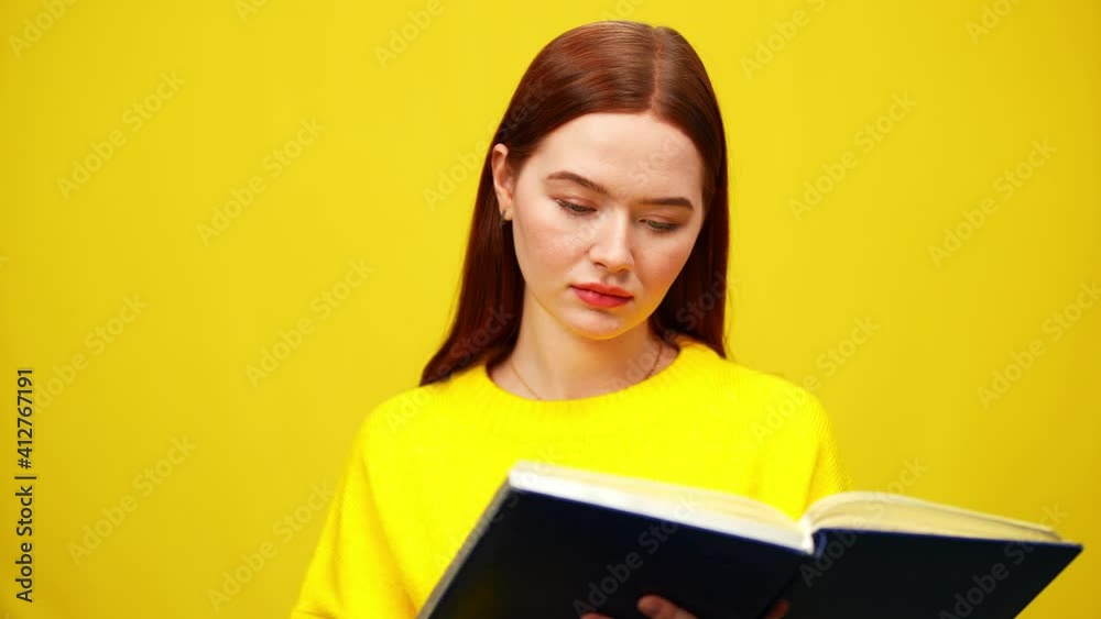 Concentrated intelligent millennial woman reading book at yellow background and smiling. Portrait of confident smart Caucasian lady enjoying literature. Lifestyle and hobby. Concentrated intelligent millennial woman reading book at yellow background and smiling. Portrait of confident smart Caucasian lady enjoying literature. Lifestyle and hobby.