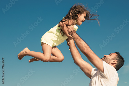 Joyful dad holding excited girl and throwing hands up in air. Handsome father and little daughter having fun outdoors, playing active games. Family outdoor activities concept