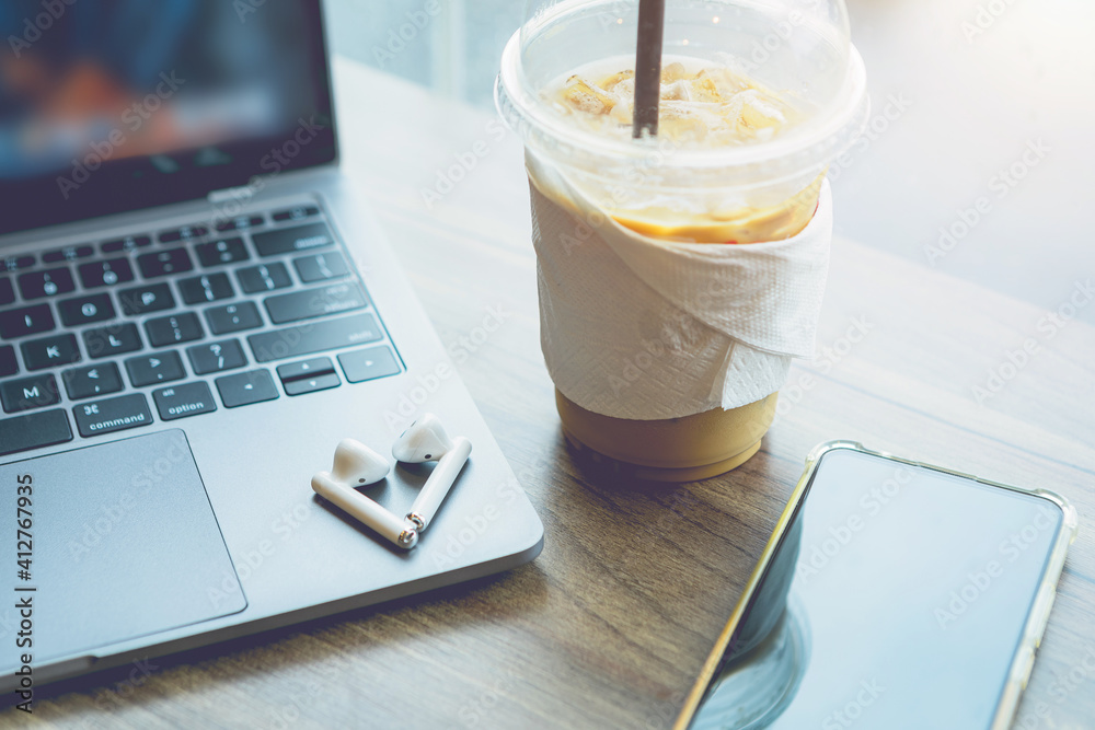 Close-up of with coffee cup working with laptop computer and earphone,smartphone with isolate on wooden office desk in coffee shop like the background Close-up of with coffee cup working with laptop computer and earphone,smartphone with isolate on wooden office desk in coffee shop like the background