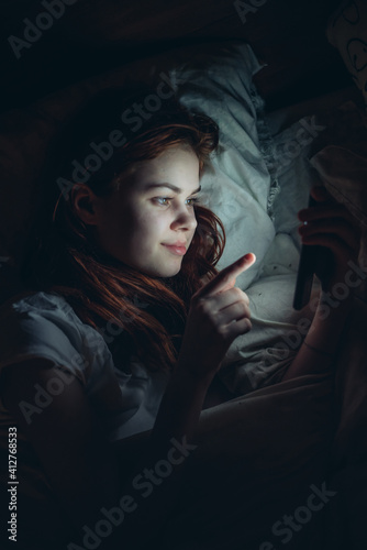 woman with a phone in her hands at night lying in bed rest before bedtime