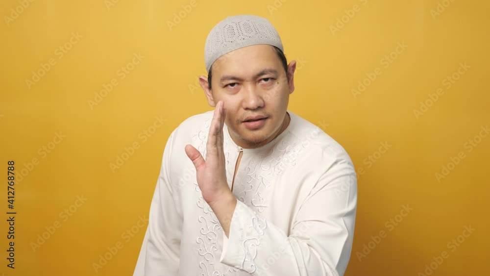 Young Asian muslim man asking to be quiet, shushing gesture, silence concept, against yellow background Young Asian muslim man asking to be quiet, shushing gesture, silence concept, against yellow background