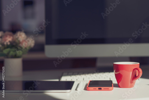 The desk with a coffee cup, tablet,  phone, computer placed.