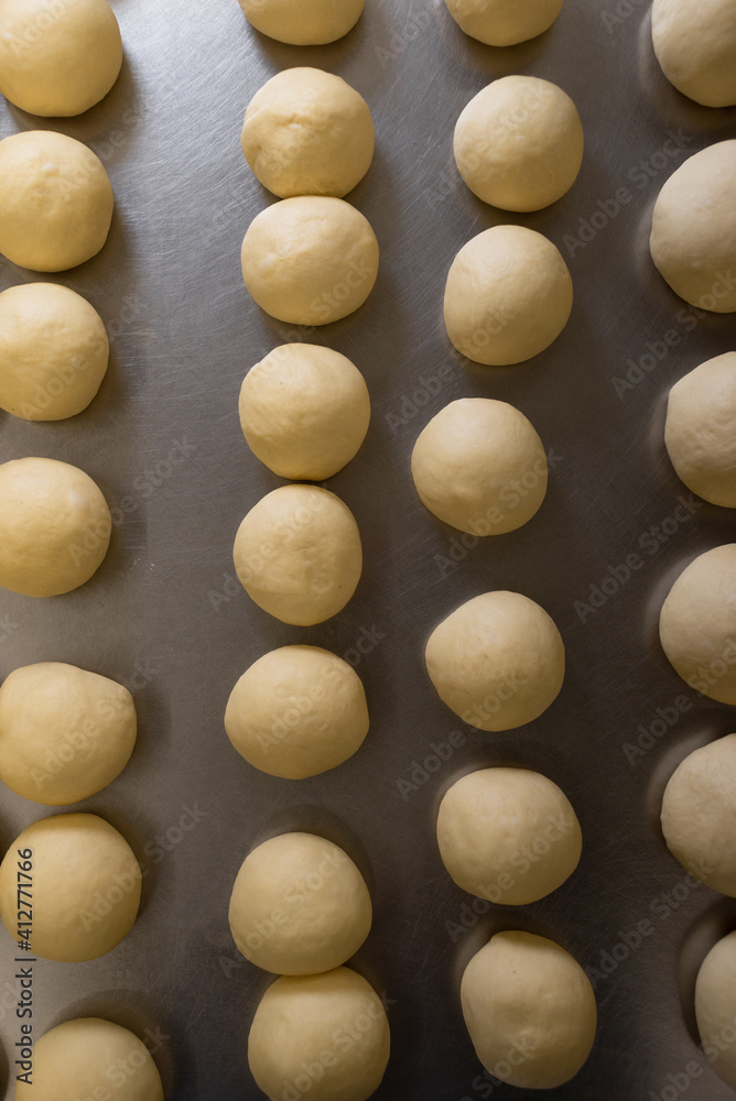 Round pieces of homemade white dough for pizza, bread or baked goods on a metal cutting board. Large dough balls are ready to bake.