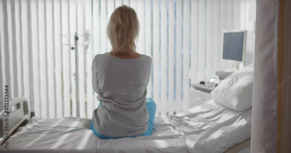 Back view of lonely mature woman sitting in bed at hospital ward Back view of lonely mature woman sitting in bed at hospital ward