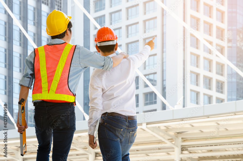 Back view engineer and technician foreman with hardhat helmet working together and viewing building in modern city. Construction, engineering and teamwork concept.