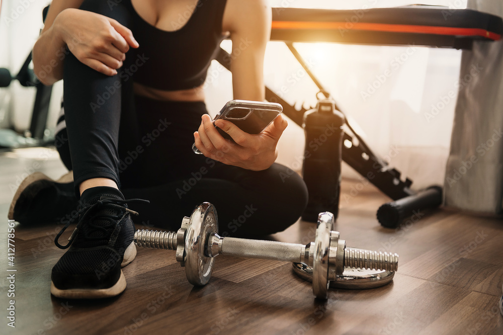Close up of woman using smart phone while workout in fitness gym. Sport and Technology concept. Lifestyles and Healthcare theme. Close up of woman using smart phone while workout in fitness gym. Sport and Technology concept. Lifestyles and Healthcare theme.