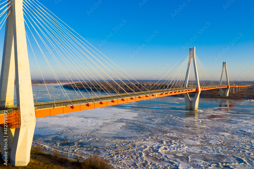 Fototapeta premium Aerial view of multispan cable-stayed Murom Bridge across ice covered Oka river on sunny winter day, Vladimir region, Russia.