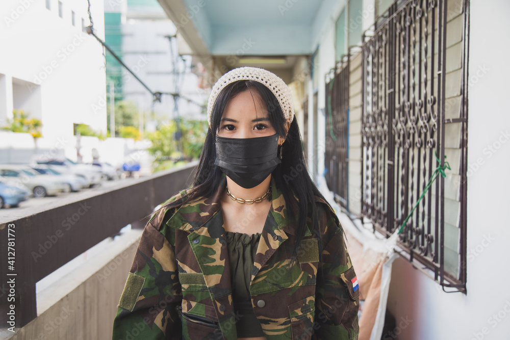 Fototapeta premium Close up portrait Asian woman in green army jacket in front of an old home apartment, Life during coronavirus pandemic.
