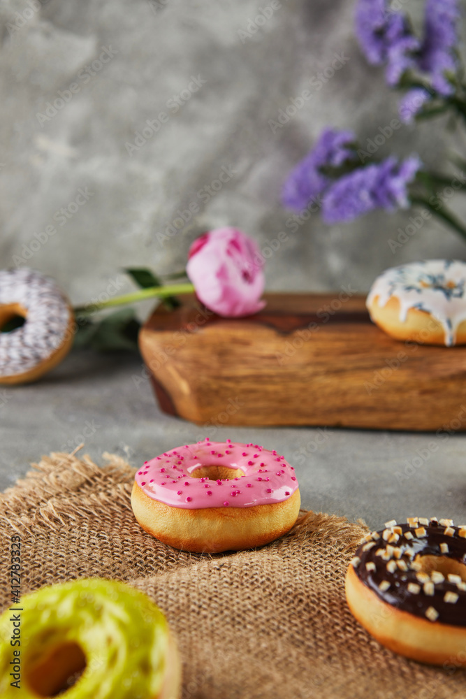 Multicolored donuts with glaze and splashes with flowers on a gray background
