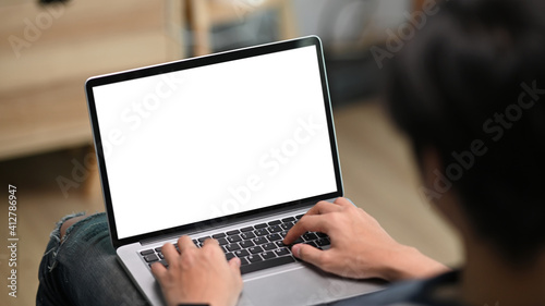 Cropped shot of young casual man using laptop computer while sitting on couch in living room.