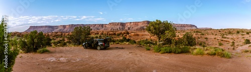 Panorama shot of camping side with blue open car fire place in american desert near canyonlands with rock massif in background in Utah