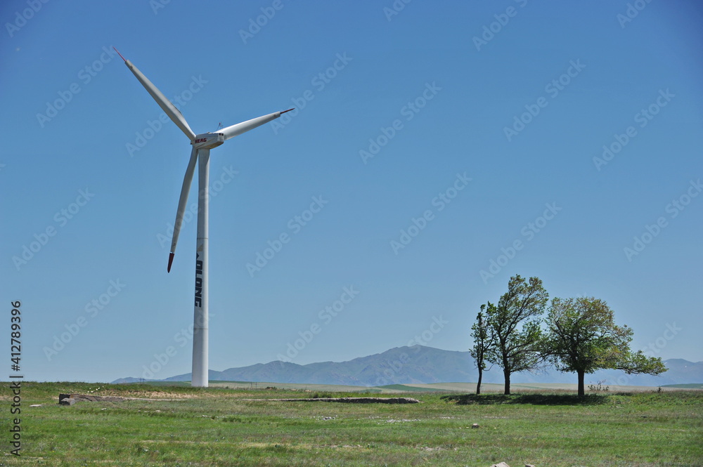 Fototapeta premium Zhambyl region, Kazakhstan - 05.15.2013 : Wind turbines located in an open hilly area with trees and grass