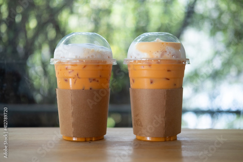 Two iced Thai milk tea in plastic cup with brown paper sleeve