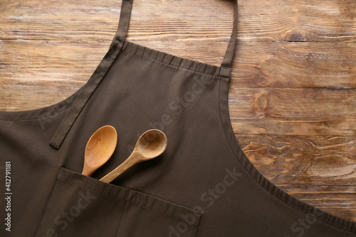 Fototapeta Clean apron and spoons on wooden background, closeup