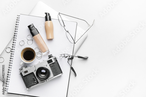 Bottles of makeup foundation, accessories and photo camera on light background