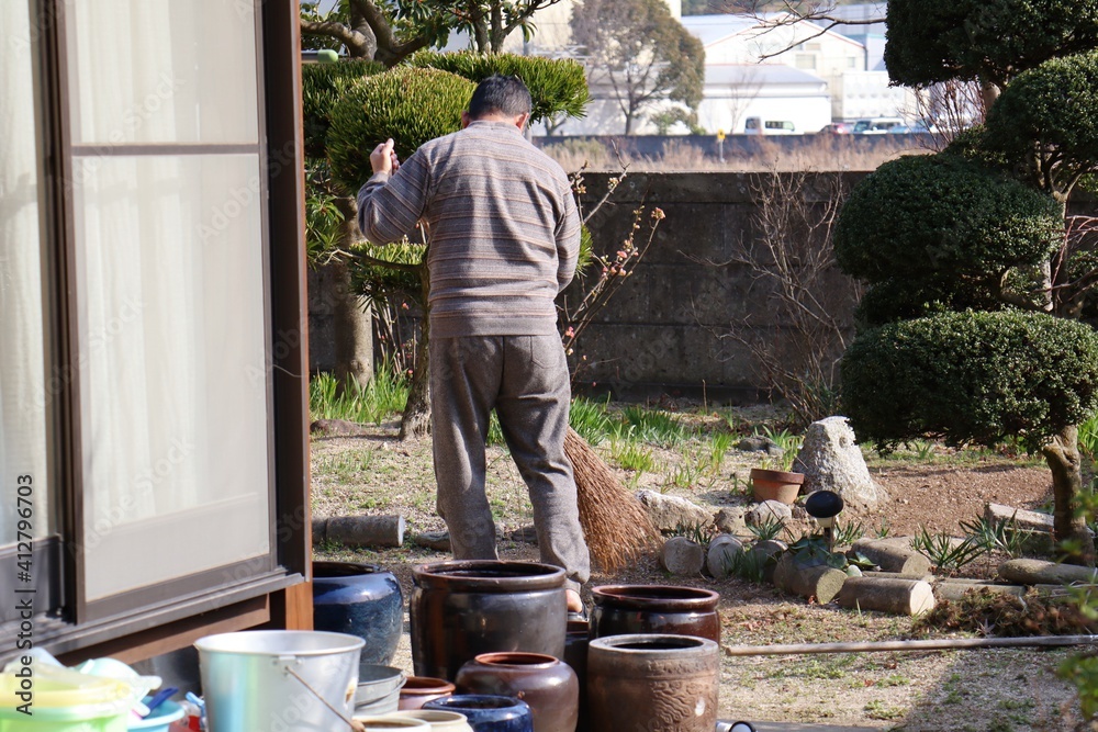 竹ぼうきで庭の掃除をする中年男性 竹ぼうきで庭の掃除をする中年男性