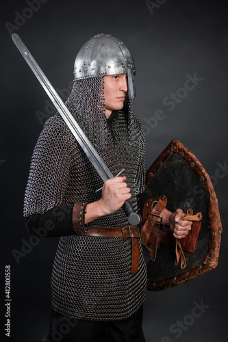 Portrait of a medieval warrior of the late Viking era and the beginning of the Crusades. Knight in chain mail and helmet armed with a shield and sword isolated on a dark background. photo