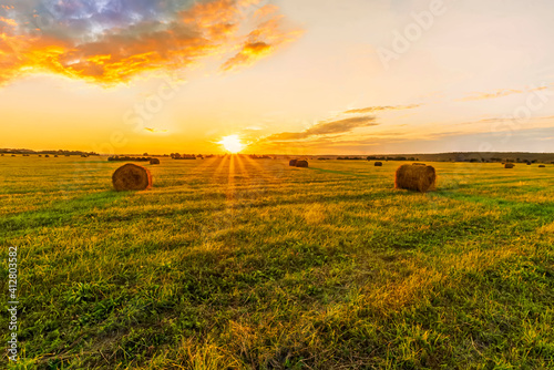 Scenic view at beautiful sunset in a green shiny field with hay stacks  cloudy sky  golden sun rays  anazing summer valley evening landscape