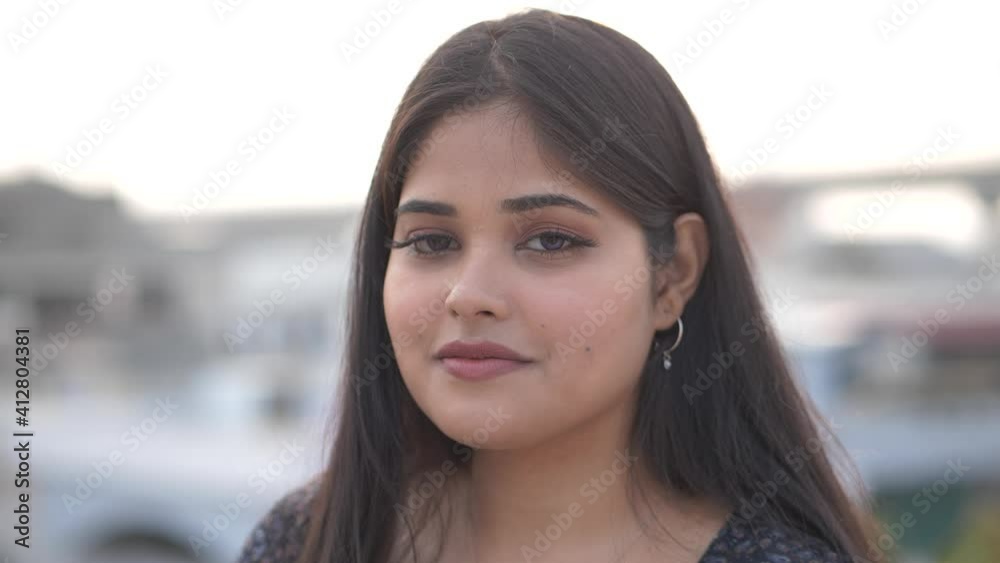 Confident young pretty Indian ethnicity woman looking at camera while standing on roof.close up face front head shot portrait.Portrait of young Asian woman smiling and looking at camera outdoors. Confident young pretty Indian ethnicity woman looking at camera while standing on roof.close up face front head shot portrait.Portrait of young Asian woman smiling and looking at camera outdoors.