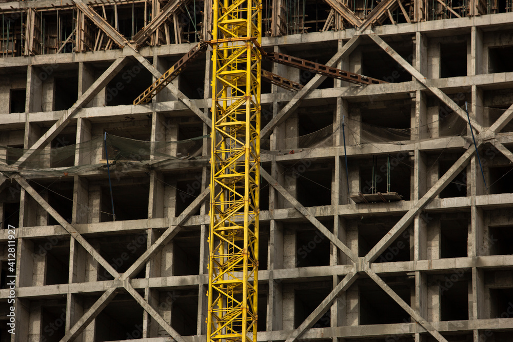 a concrete structure under construction for an apartment building. yellow tower crane goes up past the construction site of the house