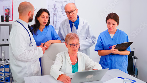 Medical practitoner working on laptop during briefing with coworkers and nurse taking notes. Clinic expert therapist talking with colleagues about disease, medicine professional photo