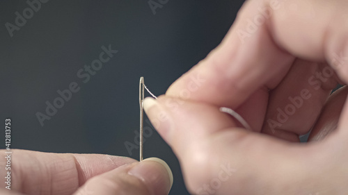 Close-up of a tailor s hands inserting a thread into the eye of a needle. Repair of clothes at home.