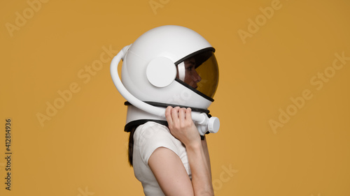 Woman with space helmet on her head on orange background. Side view. photo