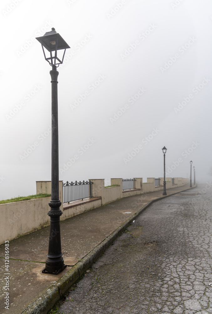 urban street in the daytime with very thick fog and mist and a row of nostalgic old black street lamps