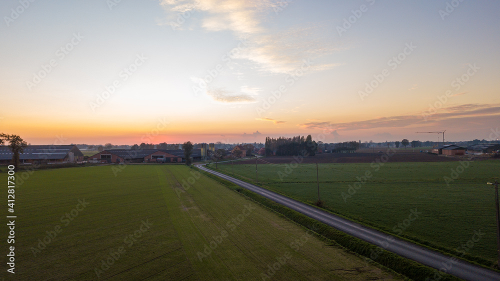 Dramatic and colorful sunrise or sunset sky over a grassy green farmfield shot from drone high up. High quality photo
