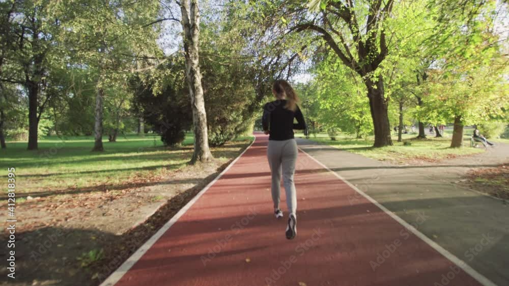 Fitness girl running on an all weather synthetic track surface over a wooden bridge in the park. Full body shot Fitness girl running on an all weather synthetic track surface over a wooden bridge in the park. Full body shot
