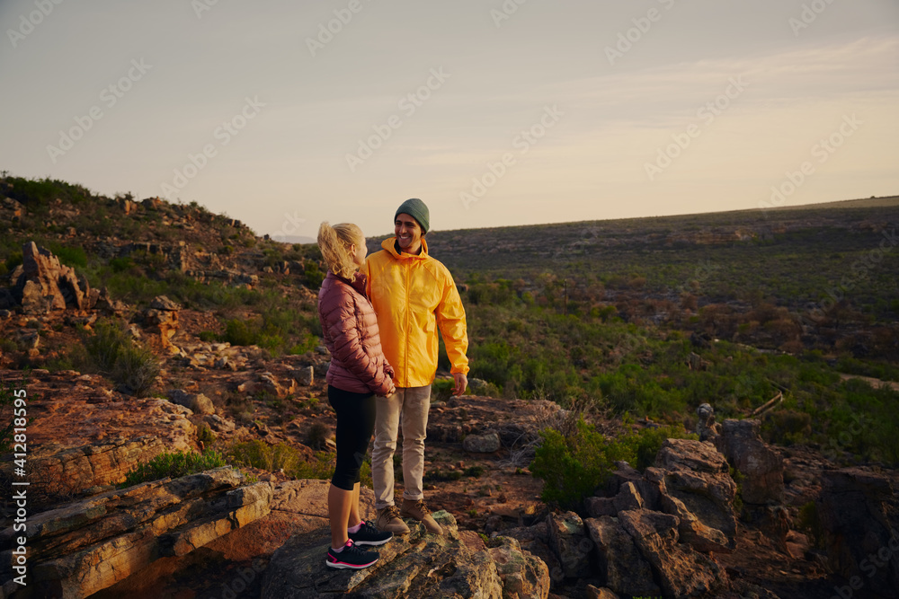 Handsome man looking at beautiful girl smiling after hiking and reaching mountain cliff edge