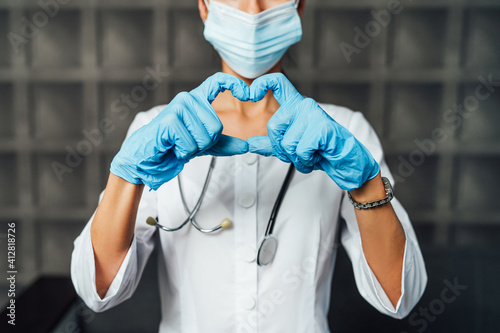 A photo of a doctor in a protective mask, with a stethoscope and in blue gloves shows his heart with his fingers. Doctor, nurse, ambulance
