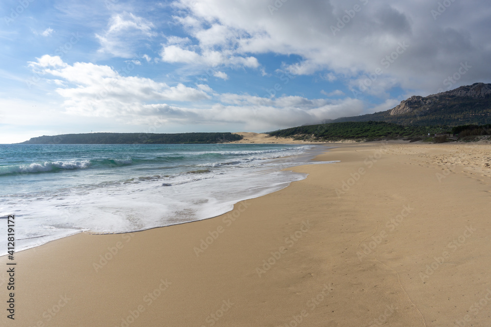 peaceful empty golden sand beach with waves rolling in and pine forest and a large sand dune in the background peaceful empty golden sand beach with waves rolling in and pine forest and a large sand dune in the background