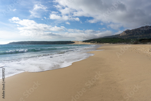 peaceful empty golden sand beach with waves rolling in and pine forest and a large sand dune in the background
