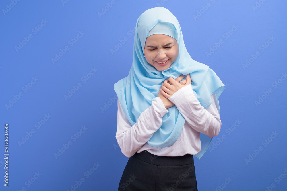 Young muslim woman wearing hijab suffering from chest pain over blue background studio, Heart attack and medical concept.