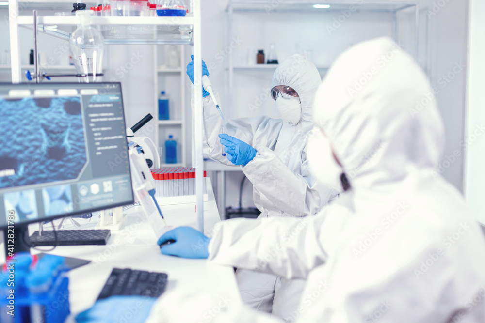 Experienced doctor taking sample from test tube using micropipette wearing sterile suit. Team of microbiologists in research laboratory conducting experiment during global pandemic with covid19. Experienced doctor taking sample from test tube using micropipette wearing sterile suit. Team of microbiologists in research laboratory conducting experiment during global pandemic with covid19.