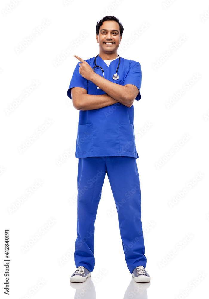 healthcare, profession and medicine concept - happy smiling indian doctor or male nurse in blue uniform with stethoscope pointing finger to something over white background healthcare, profession and medicine concept - happy smiling indian doctor or male nurse in blue uniform with stethoscope pointing finger to something over white background