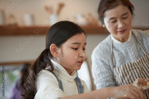 Happy adorable little child girl in apron enjoying cooking homemade pastry together with grandmother at home.