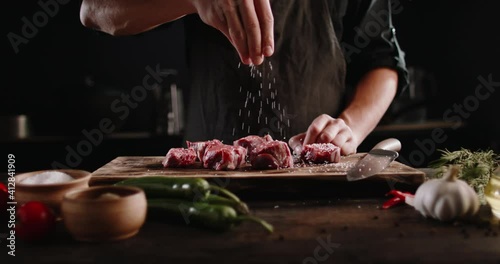 Chef cooks beef steak, sprinkling with salt on a background of professional kitchen, slow motion